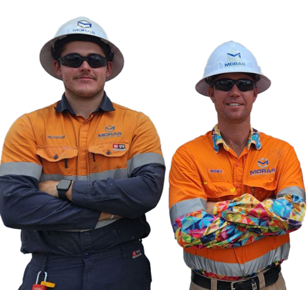 Two people wearing orange safety uniforms and white hard hats stand side by side with arms crossed. Both have dark sunglasses. The uniform has a logo and names, indicating they are likely in a work or industrial setting.